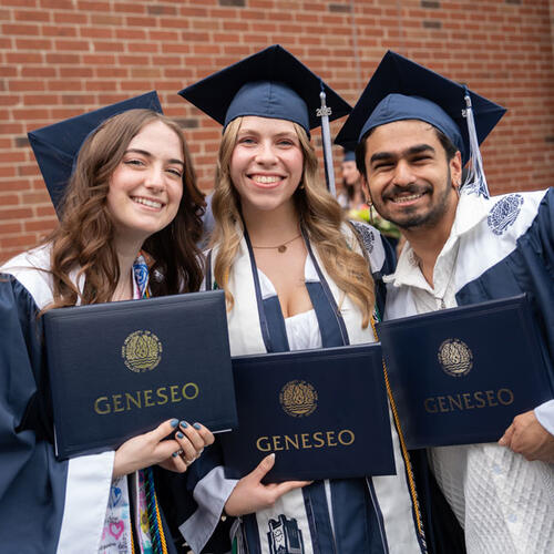three graduates holding diplomas